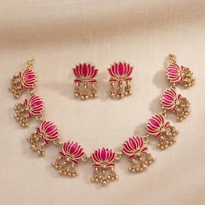 May include: A gold-toned necklace and matching earring set featuring multiple lotus flower motifs. Each lotus is filled with vibrant pink enamel and accented with small, dangling gold-toned beads attached to the base of every flower element.