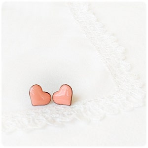 Pode incluir: Um par de brincos em forma de coração cor de pêssego em um fundo branco.