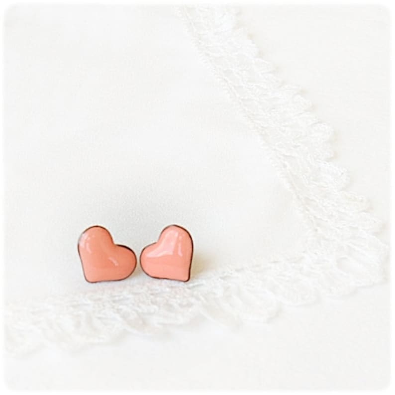 May include: A pair of peach-colored heart-shaped earrings on a white background.