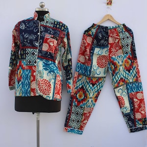 May include: A long-sleeved button-down shirt and matching trousers set featuring a vibrant patchwork pattern of red, blue, white, and yellow floral and geometric motifs. The shirt has a collar and white buttons, while the trousers have an elastic waistband.