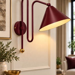 May include: A wall-mounted lamp featuring a deep burgundy, S-shaped metal arm and a matching conical shade with a white interior. The fixture includes a circular wall plate and a small, spherical gold-toned accent at the base of the vertical arm.