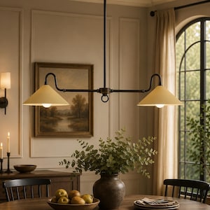 Peut inclure: Un luminaire suspendu linéaire doté d'une structure en métal bronze foncé avec deux abat-jours coniques orientés vers le bas de couleur crème. Le luminaire est suspendu par une tige centrale et comprend deux ampoules sous les abat-jours.