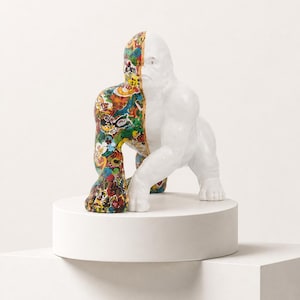 Puede incluir: Una escultura de gorila con un diseño dividido. Una mitad es de color blanco sólido con un acabado liso, mientras que la otra mitad está cubierta por un collage vibrante y multicolor de varias ilustraciones gráficas, patrones e imágenes.