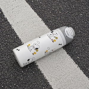 May include: A white cylindrical water bottle featuring a repeating pattern of Snoopy and Woodstock characters with yellow flowers and black bone icons. The bottle has a gray lid with a push-button mechanism and the text Push Button printed on it.