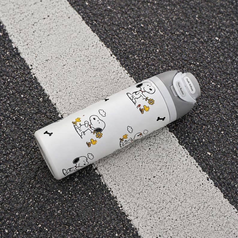 May include: A white cylindrical water bottle featuring a repeating pattern of Snoopy and Woodstock characters with yellow flowers and black bone icons. The bottle has a gray lid with a push-button mechanism and the text Push Button printed on it.