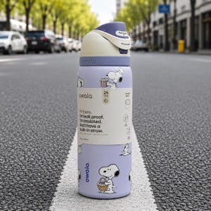 May include: A light purple Owala insulated water bottle featuring Snoopy graphics, a cream-colored push-button lid, and a built-in straw. The bottle includes a product label stating 24 hours cold and 24 oz / 710 mL capacity with leak-proof features.