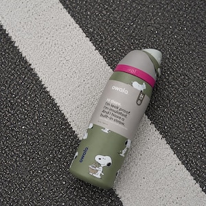 May include: An olive green Owala water bottle with a Snoopy pattern, a dark gray lid, and a bright pink band. The label reads: Hi there. I'm leak proof. I'm insulated. And I have a built-in straw. It has a capacity of 32 oz / 945 ml.