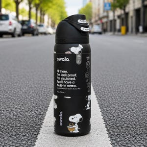 May include: A black Owala insulated water bottle with a 32 oz capacity, featuring a built-in straw, a push-button lid, and a Snoopy graphic print. The bottle displays text stating, Hi there. I'm leak proof. I'm insulated. And I have a built-in straw.