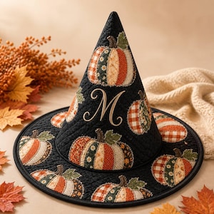 May include: A black quilted witch hat featuring an embroidered letter M in the center. The hat is decorated with multiple fabric pumpkin appliques in shades of orange, green, and cream, showcasing various patterns like plaid and floral prints.