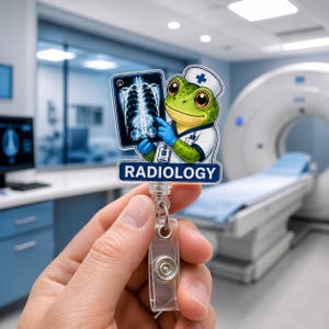May include: A badge reel featuring a cartoon green frog dressed as a medical professional wearing a white cap with a blue cross, holding a chest X-ray image. Below the frog, a blue rectangular sign displays the white text RADIOLOGY.