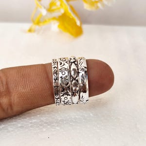 Könnte beinhalten: Ein Set aus vier silberfarbenen Metallringen mit komplexen Prägemustern. Jeder Ring zeigt ein eigenes Design, darunter florale Motive, geometrische Formen und lineare Gravuren, die alle mit einem dunklen Oxydationseffekt versehen sind.