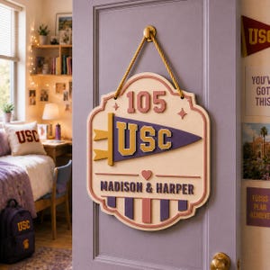 May include: A decorative wooden wall sign hanging from a gold rope on a door. The sign features the number 105, a purple and gold USC pennant graphic, and the names Madison & Harper in purple lettering, accented with a small heart and vertical stripes.