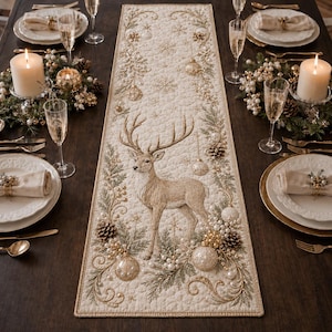 May include: A rectangular cream-colored table runner featuring an embroidered brown deer standing in the center, surrounded by intricate gold and green pine branches, pinecones, pearl-like beads, and hanging Christmas ornament designs.