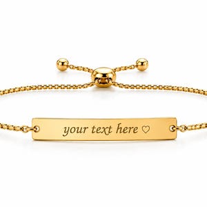 Op de afbeelding: Een goudkleurige, verstelbare armband met een dunne boxketting en een centrale rechthoekige staaf. De staaf is gegraveerd met de tekst "your text here" gevolgd door een klein hartsymbool. De armband heeft een schuifsluiting met kraal.