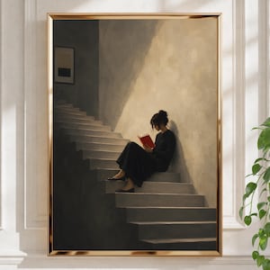 Op de afbeelding: Een ingelijste muurkunstprint met een persoon in een zwarte jurk die op een trap zit en een felrood boek leest. De scène toont een contrastrijk spel van licht en schaduw tegen een getextureerde muur, met een kleine ingelijste afbeelding.