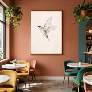 May include: A framed wall art print featuring a delicate, fine-line ink drawing of a hummingbird in flight. The bird is rendered in thin, flowing black lines against a solid, light cream-colored background, capturing the motion of its wings.