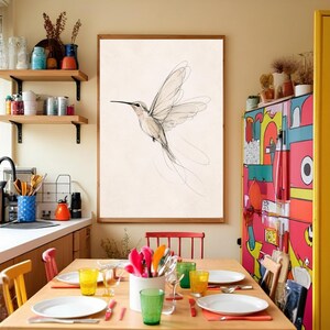 May include: A framed wall art print featuring a black ink line drawing of a hummingbird in flight against a cream background. The artwork is displayed on a light-colored wall in a kitchen setting with wooden shelves and a colorful refrigerator.