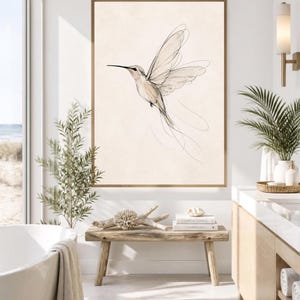 May include: A framed wall art print featuring a delicate, minimalist line drawing of a hummingbird in flight. The bird is rendered in fine black ink strokes against a solid, light beige background, capturing the motion of its wings.