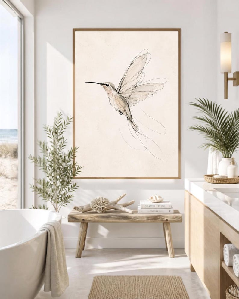 May include: A framed wall art print featuring a delicate, minimalist line drawing of a hummingbird in flight. The bird is rendered in fine black ink strokes against a solid, light beige background, capturing the motion of its wings.