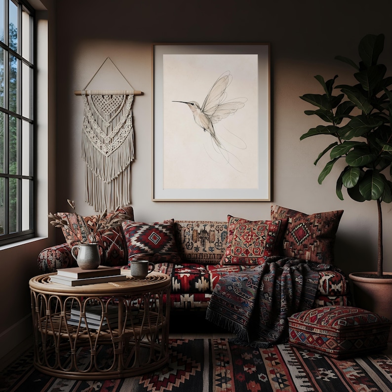 May include: A framed wall art print featuring a delicate line drawing of a hummingbird in flight, displayed in a room with a patterned sofa, a round rattan coffee table, a macrame wall hanging, and a large potted plant on the floor.