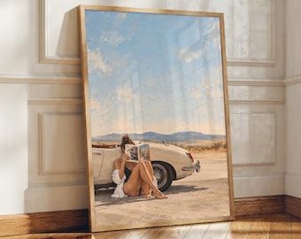 Peut inclure: Une impression d'art encadrée représentant une personne en maillot de bain noir et chemise blanche assise par terre en train de lire un livre à côté d'une voiture décapotable crème vintage dans un paysage désertique sous un ciel bleu nuageux.