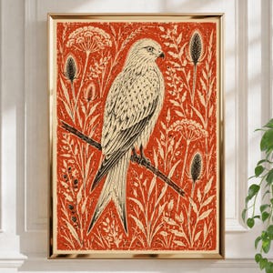 Op de afbeelding: Een ingelijste print met een zwart-witte linosnede-illustratie van een roofvogel op een tak, tegen een levendige oranje achtergrond vol gedetailleerde botanische elementen zoals distels en bloeiende schermbloemen.