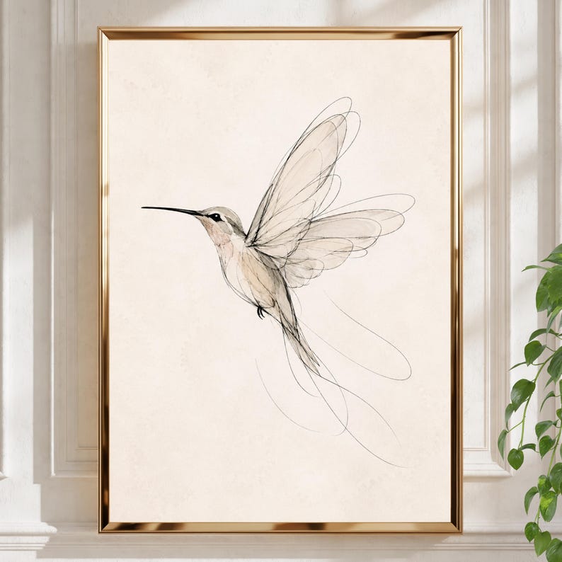 May include: A framed wall art print featuring a delicate line drawing of a hummingbird in flight. The bird is rendered in fine black ink strokes against a solid, light beige background, captured within a thin, metallic gold-colored frame.