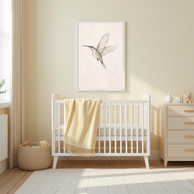 May include: A framed wall art print featuring a delicate black line drawing of a hummingbird in flight against a light cream background, displayed above a white wooden crib with a soft yellow throw blanket draped over the side rail.
