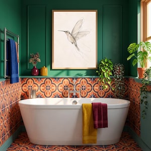 May include: A framed wall art print featuring a delicate line drawing of a hummingbird in flight, displayed above a white freestanding bathtub in a bathroom with green walls and patterned orange and blue tiles on the lower wall sections.
