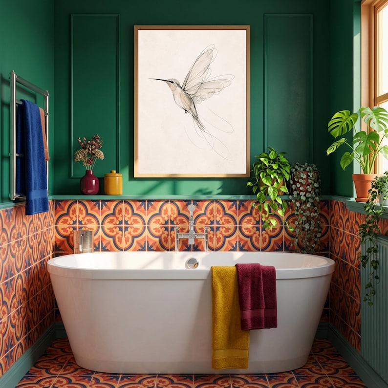 May include: A framed wall art print featuring a delicate line drawing of a hummingbird in flight, displayed above a white freestanding bathtub in a bathroom with green walls and patterned orange and blue tiles on the lower wall sections.