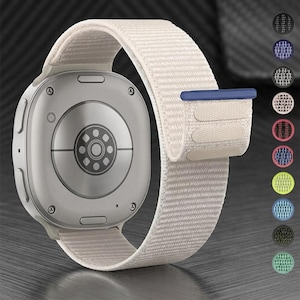 May include: A smartwatch with a light beige fabric strap featuring a dark blue tab. The back of the watch case is silver with a circular sensor array. A vertical column of eleven small circular color swatches is displayed to the right side.