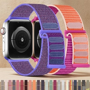 Könnte beinhalten: Eine silberne Smartwatch mit einem violetten, gewebten Nylon-Sportarmband mit Klettverschluss. Ein zweites orange-pinkes, gewebtes Nylonarmband befindet sich hinter der Uhr, und eine Farbpalette mit verschiedenen Armbandoptionen ist unten abgebildet.