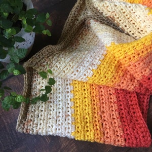 以下が含まれることがあります： 茶色から始まり、クリーム色、黄色、オレンジ、赤へとグラデーションになる、かぎ針編みの毛布。毛布は、テクスチャのあるステッチで編まれています。