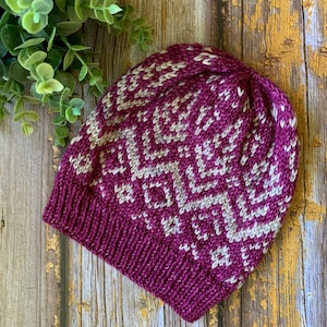 May include: A purple and white knitted hat with a geometric pattern. The hat is made with a soft yarn and has a comfortable fit.