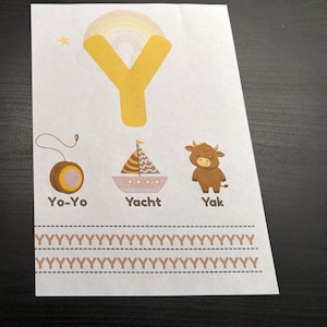 Op de afbeelding: Een wit educatief blad met een grote gele letter Y met een regenboog op de achtergrond. Daaronder staan illustraties van een bruine jojo, een zeilboot met het label Yacht en een bruine jak. Onderaan staan twee rijen van de letter Y in bruin.
