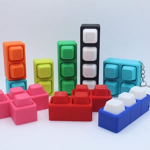 Könnte beinhalten: Eine Sammlung bunter Silikon-Fidget-Spielzeuge in Form von mechanischen Tastaturschaltern in verschiedenen Formen und Konfigurationen. Das Set enthält orange, gelbe, grüne, schwarze, rosa, rote, blaue und türkisfarbene Blöcke mit Tastenkappen.