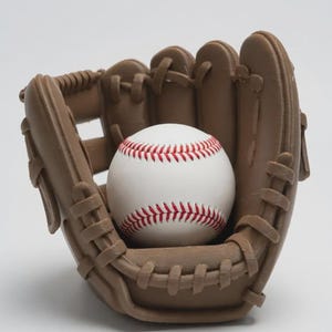 May include: A baseball and glove set. The baseball is white with red stitching, nestled inside a brown baseball glove. The glove has a classic design with visible stitching and a pocket to catch the ball. The background is plain white.