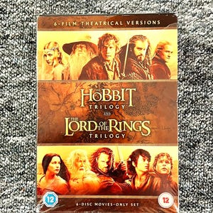 Puede incluir: Un set de 6 discos que incluye la trilogía de El Hobbit y la trilogía de El Señor de los Anillos. La portada muestra personajes de las películas sobre un fondo de mapa con el texto 6-Film Theatrical Versions y 6-Disc Movies-Only Set con logos de 12.