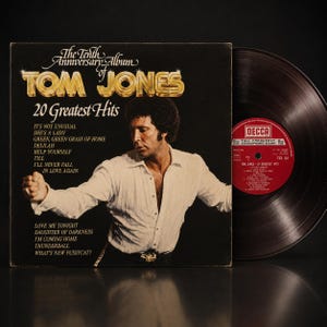Peut inclure: Pochette d'album vinyle vintage de Tom Jones, "20 Greatest Hits". La couverture présente une photo de Tom Jones en chemise blanche. Le titre de l'album est en lettres dorées. Le disque est noir avec une étiquette rouge.