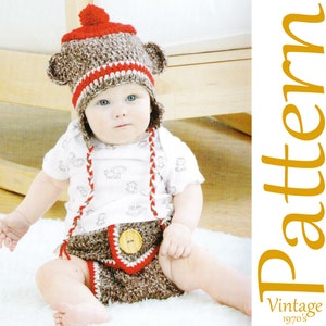 May include: A baby wearing a handmade crochet monkey hat and diaper cover set. The hat is brown and red with ear details and a pom-pom. The diaper cover has a wooden button and red trim. The baby is wearing a white onesie with monkey graphics.