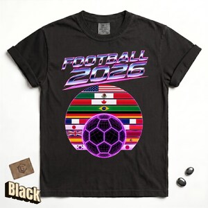 May include: A black short-sleeve t-shirt featuring the text FOOTBALL 2026 in a metallic purple and silver font. Below the text is a circular graphic containing various national flags and a glowing purple wireframe soccer ball in the center.