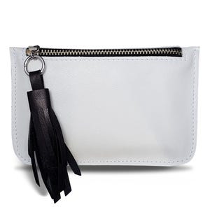 Puede incluir: Clutch rectangular blanca con cremallera negra y borla de cuero negro. El clutch está hecho de un material liso y tiene un diseño minimalista. La cremallera es plateada.