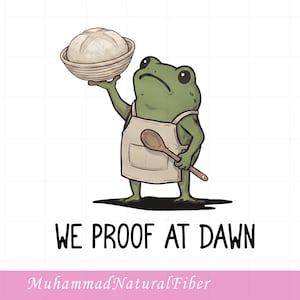 May include: A green frog illustration wearing a beige apron, holding a wooden spoon and a round loaf of bread in a proofing basket. The text WE PROOF AT DAWN is printed below the frog, with the text MuhammadNaturalFiber at the bottom.