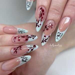 Könnte beinhalten: Mandelformige Fingernägel mit nudefarbener Basis und weißen French-Spitzen. Das Design zeigt handgemalte dunkelrote Kirschblütenzweige, die von den Spitzen ausgehen, sowie schwarze japanische Kanji-Schriftzeichen auf den weißen Spitzen.