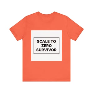 Peut inclure: Un t-shirt à manches courtes de couleur corail vif avec un motif carré blanc centré. À l'intérieur du carré, un cadre rectangulaire noir entoure le texte en gras brun foncé qui indique SCALE TO ZERO SURVIVOR dans une police sans empattement.