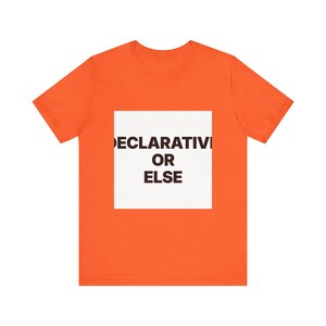 Peut inclure: Un t-shirt orange vif à manches courtes avec un carré blanc centré sur la poitrine. À l'intérieur du carré blanc, le texte DECLARATIVE OR ELSE est imprimé en lettres capitales grasses, brun foncé et sans empattement sur trois lignes.