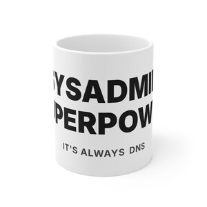 Peut inclure: Tasse en céramique blanche avec l'inscription "SYSADMIN SUPERPOWER" en grosses lettres noires. En dessous, en plus petit, on peut lire "IT'S ALWAYS DNS". Un design simple et audacieux pour les passionnés de technologie.
