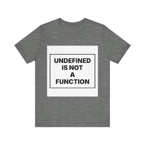 Peut inclure: Un t-shirt gris chiné à manches courtes avec un motif carré blanc sur la poitrine. À l'intérieur du carré, une bordure rectangulaire noire encadre le texte noir en gras qui indique : UNDEFINED IS NOT A FUNCTION en police sans empattement.