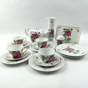 Könnte beinhalten: Ein Teeservice aus weißem Porzellan mit handgemaltem Blumenmotiv in leuchtendem Pink und Grün. Das Set besteht aus einer Teekanne, einer hohen Vase, einem rechteckigen Tablett, einer Zuckerdose mit Deckel sowie mehreren Tassen und Untertassen.