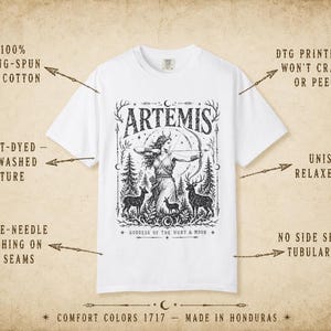 May include: White t-shirt with a black graphic of Artemis, the Greek goddess of the hunt, with a bow and arrow, surrounded by deer and trees. The word "ARTEMIS" is at the top. The shirt is made of ring-spun cotton and has a unisex relaxed fit.